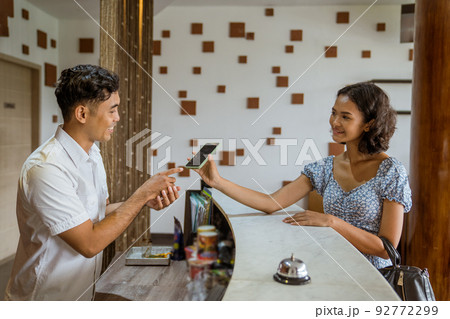 Female guest showing smartphone at receptionist for proof of booking 92772299