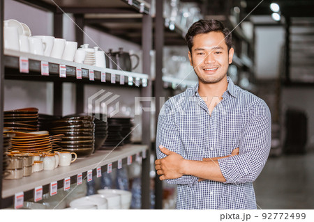 Handsome asian man standing with hands crossed standing beside shelf 92772499