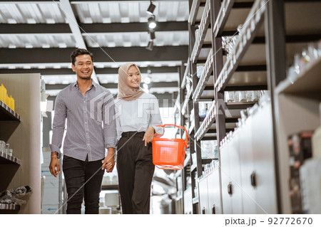 Asian muslim young couple carrying baskets walking between shelves 92772670