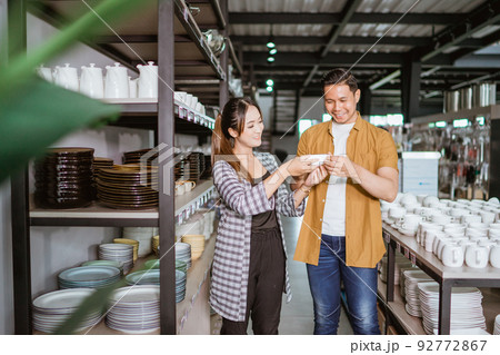 Young asian woman and young man holding ceramic cups choosing 92772867