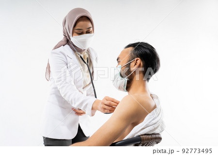 Masked doctor using a stethoscope examining prospective pilgrims 92773495