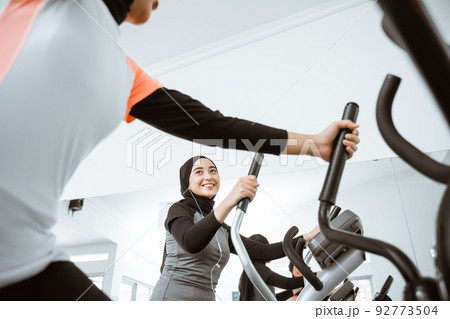 woman with hijab exercising with friend on static elliptical cycle machine woman with hijab exercising with friend on static elliptical cycle machine 92773504