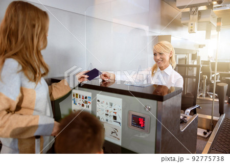 Young woman giving passport back to lady with kid at airport check in Young woman giving passport back to lady with kid at airport check in 92775738