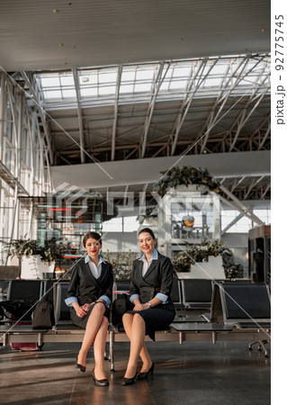 Two flight attendants sitting on the seats in the airport terminal Two flight attendants sitting on the seats in the airport terminal 92775745