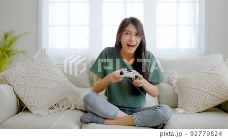 Beautiful young asian woman sitting on sofa and holding joystick playing online video game 92779824