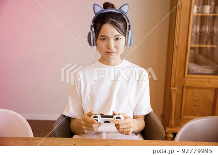 猫耳ヘッドフォンをして家でゲームをする若い女性 92779995
