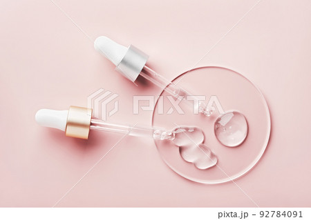 Two pipettes with different samples of gels cosmetic products in petri dish on pink background Two pipettes with different samples of gels cosmetic products in petri dish on pink background 92784091