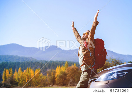 Man with arms raised up cheerful and happy sitting on car. Tourist with backpack enjoy mountain views Man with arms raised up cheerful and happy sitting on car. Tourist with backpack enjoy mountain views 92785066
