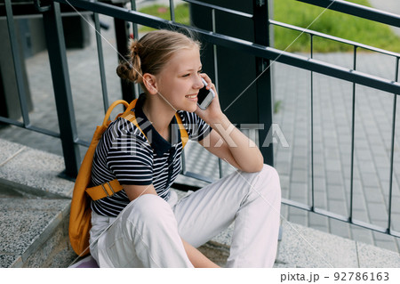 A beautiful girl is sitting on the stairs at school in between classes and talking on the phone A beautiful girl is sitting on the stairs at school in between classes and talking on the phone 92786163