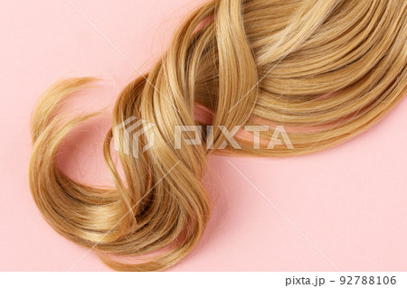 Long golden blond curly hair. A part of blond hair top view on pink background. 92788106