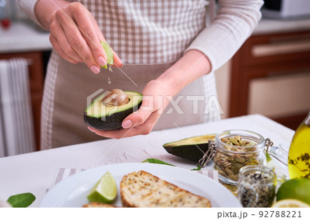 Woman squeezing fresh lime juice on a halved avocado at domestic kitchen Woman squeezing fresh lime juice on a halved avocado at domestic kitchen 92788221
