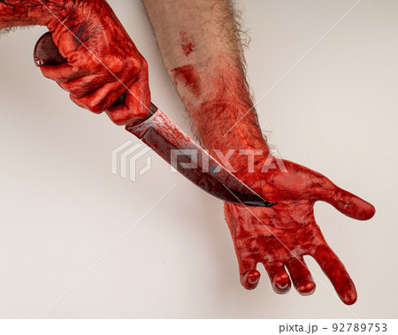 A man with bloody hands cuts himself with a knife. 92789753