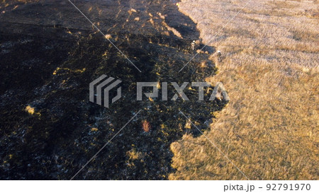 Aerial view Fire extinguishing. Fireman extinguishing burning dry grass. Open flames of fire and smoke. Yellow dry grass and black ash from burnt plants.Ecological catastrophy. Fire on field in steppe 92791970