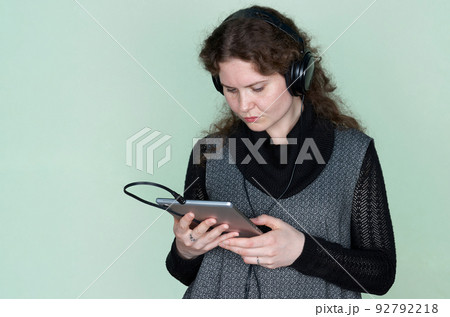 A woman with curly hair carefully looks at a digital tablet that she holds in her hands 92792218
