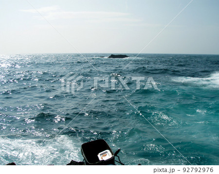 真夏の西伊豆、磯釣り用コマセバッカンの置かれた磯際からサラシの伸びる雄大な駿河湾を望む風景写真。 92792976