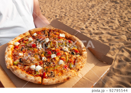 Pizza with mushrooms, tomatoes and mozzarella lies in brown paper box in male hands 92795544