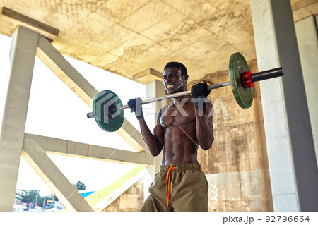 Athletic black young man lifting a heavy-weight barbell in outdoor gym under the bridge. Healthy lifestyle concept Athletic black young man lifting a heavy-weight barbell in outdoor gym under the bridge. Healthy lifestyle concept 92796664