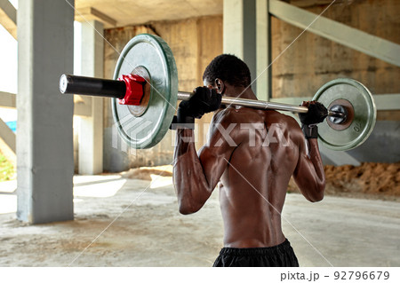 Athletic black young man lifting a heavy-weight barbell in outdoor gym under the bridge. Healthy lifestyle concept Athletic black young man lifting a heavy-weight barbell in outdoor gym under the bridge. Healthy lifestyle concept 92796679