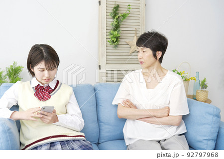 自宅で母親に叱られるスマホを使う女子高生 92797968