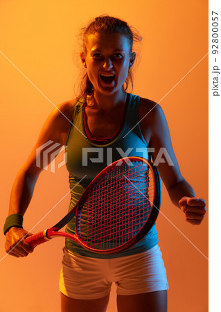 Portrait of woman, professional tennis player training isolated over orange studio background in neon light. Growing motivation 92800057