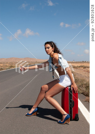 attractive woman hitchhiking on a lonely road attractive woman hitchhiking on a lonely road 92801628