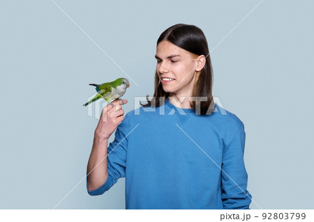 Portrait of young male with green parrot on his hand on gray background 92803799