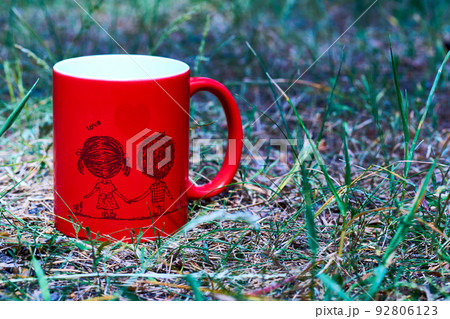 Red ceramic cup inscription love and funny couple on green grass in the park Red ceramic cup inscription love and funny couple on green grass in the park 92806123