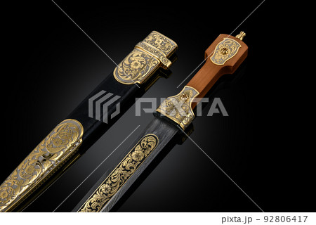 souvenir collectible silver gold dagger cutlass with scabbard, with metal engraving, on black background. Luxury weapons with traditional patterns in medieval vintage style. souvenir collectible silver gold dagger cutlass with scabbard, with metal engraving, on black background. Luxury weapons with traditional patterns in medieval vintage style. 92806417