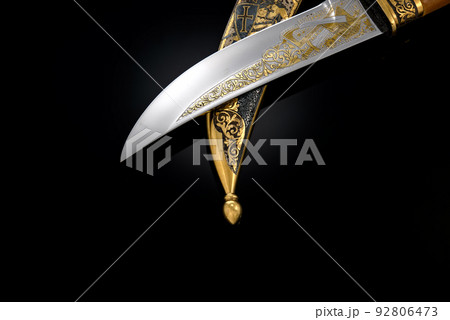 souvenir collectible silver gold dagger cutlass with scabbard, with metal engraving, on black background. Luxury weapons with traditional patterns in medieval vintage style. souvenir collectible silver gold dagger cutlass with scabbard, with metal engraving, on black background. Luxury weapons with traditional patterns in medieval vintage style. 92806473