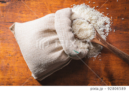 Uncooked white rice in burlap sack on wooden table. 92806589