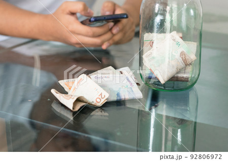 man doing online shopping, bad financial situation, guy texting on his mobile phone, banknotes on the table, bankrupt young man, spending his savings. economic concept man doing online shopping, bad financial situation, guy texting on his mobile phone, banknotes on the table, bankrupt young man, spending his savings. economic concept 92806972