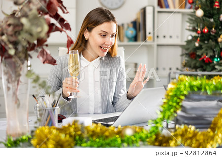 Woman manager with glass of champagne having video call conversation in Christmas decorated office Woman manager with glass of champagne having video call conversation in Christmas decorated office 92812864