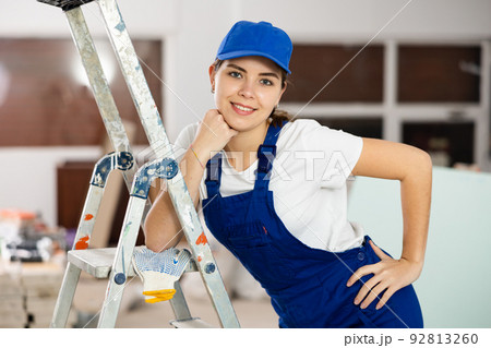 Smiling young female builder in blue uniform at construction site Smiling young female builder in blue uniform at construction site 92813260