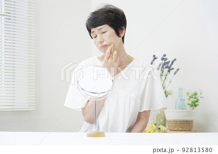リビングで鏡で顔を見て悩むシニア女性 リビングで鏡で顔を見て悩むシニア女性 92813580