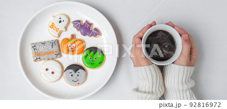 woman hand holding coffee cup during eating funny Halloween Cookies. Happy Halloween day, Trick or Threat, Hello October, fall autumn, Traditional, party and holiday concept 92816972