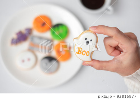 woman hand holding funny Halloween Cookie during drinking coffee. Happy Halloween day, Trick or Threat, Hello October, fall autumn, Traditional, party and holiday concept 92816977