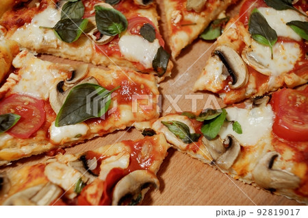 Close-up of an appetizing, freshly baked vegetarian pizza with addition ripe juicy tomatoes, organic champignons and aromatic basil herbs, divided into portions on a wooden background. Selective focus Close-up of an appetizing, freshly baked vegetarian pizza with addition ripe juicy tomatoes, organic champignons and aromatic basil herbs, divided into portions on a wooden background. Selective focus 92819017