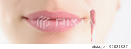 Brush with pink matte lip gloss on background face, close-up 92821327