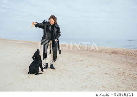 Woman wearing black coat plays with her dog 92826811