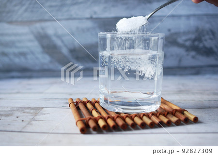 pouring white sugar in a glass of water on table  92827309