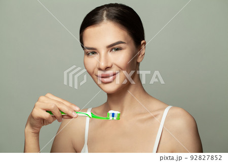 Beautiful young woman with green toothbrush on light green background Beautiful young woman with green toothbrush on light green background 92827852