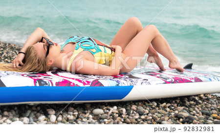sexy girl is lying on a sup board by the sea in beautiful stylish summer clothes 92832981