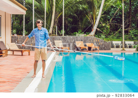 Cleaner of the swimming pool . Man in a blue shirt with cleaning equipment for swimming pools, sunny 92833064
