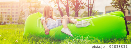 Young woman resting on an air sofa in the park. BANNER, long format 92833331