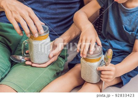 Father and son eat dessert with chia seeds and mangoes by the pool in the morning. healthy eating, vegetarian food, diet and people concept 92833423