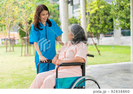 Asian careful caregiver or nurse hold the patient hand and encourage the patient in a wheelchair.  Concept of happy retirement with care from a caregiver and Savings and senior health insurance. 92838860