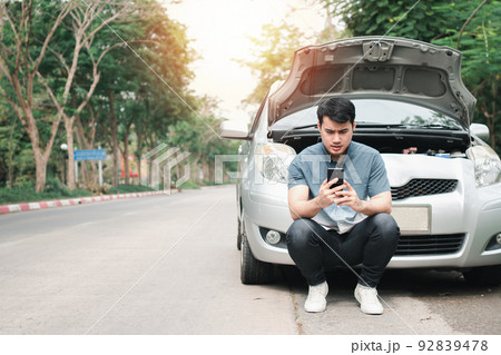 Asian man using mobile phone calling for assistance after a car breakdown on street. Concept of vehicle engine problem or accident and emergency help from Professional mechanic Asian man using mobile phone calling for assistance after a car breakdown on street. Concept of vehicle engine problem or accident and emergency help from Professional mechanic 92839478