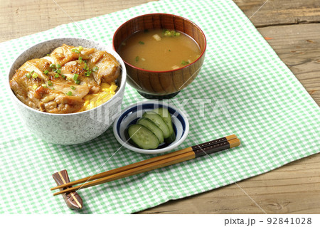 玉子焼に大きい鶏肉が乗っている照り焼きチキン丼とお味噌汁とお漬物 92841028