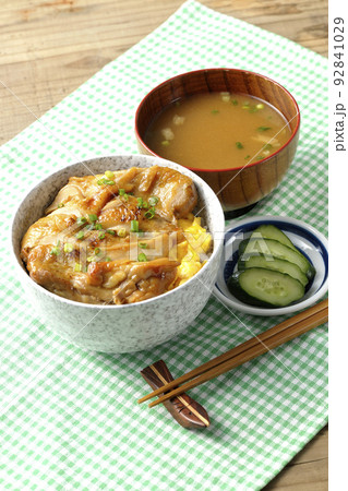 玉子焼に大きい鶏肉が乗っている照り焼きチキン丼とお味噌汁とお漬物 92841029