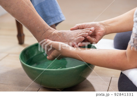 Female caregiver wipes the elderly woman feet by towel. Female caregiver wipes the elderly woman feet by towel. 92841331